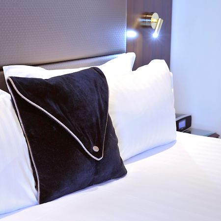 Stamford Plaza Melbourne Hotel Exterior foto The photo shows a neatly arranged bed with white linens. There are several pillows, with one black pillow featuring a distinctive design on top of the white pillows. The headboard of the bed is visible, along with a stylish wall-mounted light fixture