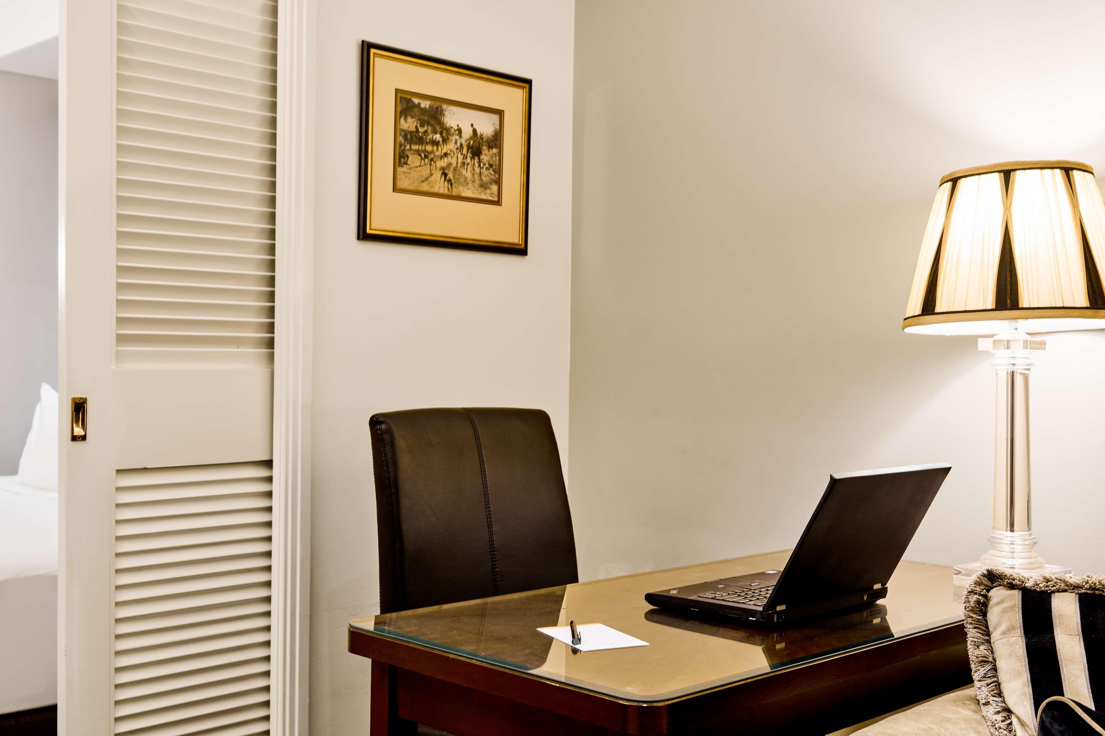 Stamford Plaza Melbourne Hotel Exterior foto The photo shows a small office or workspace. There is a desk with a glass surface, and on it sits a laptop computer. A piece of paper or notecard is also placed on the desk. Behind the desk is a black office chair. A wall lamp with a striped shade is