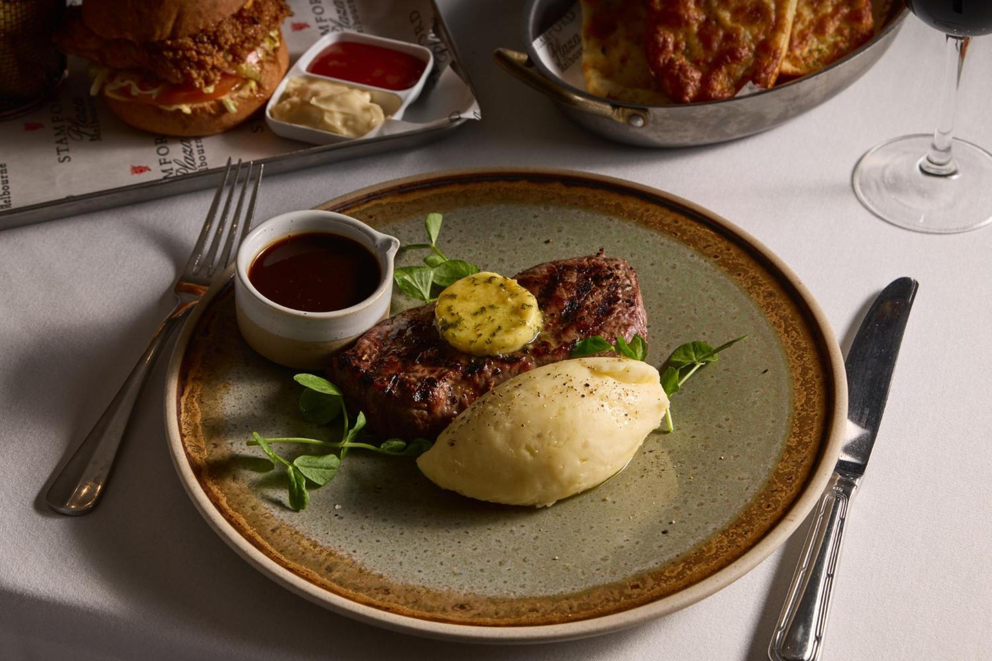 Stamford Plaza Melbourne Hotel Exterior foto The photo shows a well-presented plate featuring a serving of steak, topped with a dollop of herb butter and surrounded by fresh sprouts or microgreens. There is a smooth portion of mashed potatoes beside the steak, and a small bowl of sauce, likely 