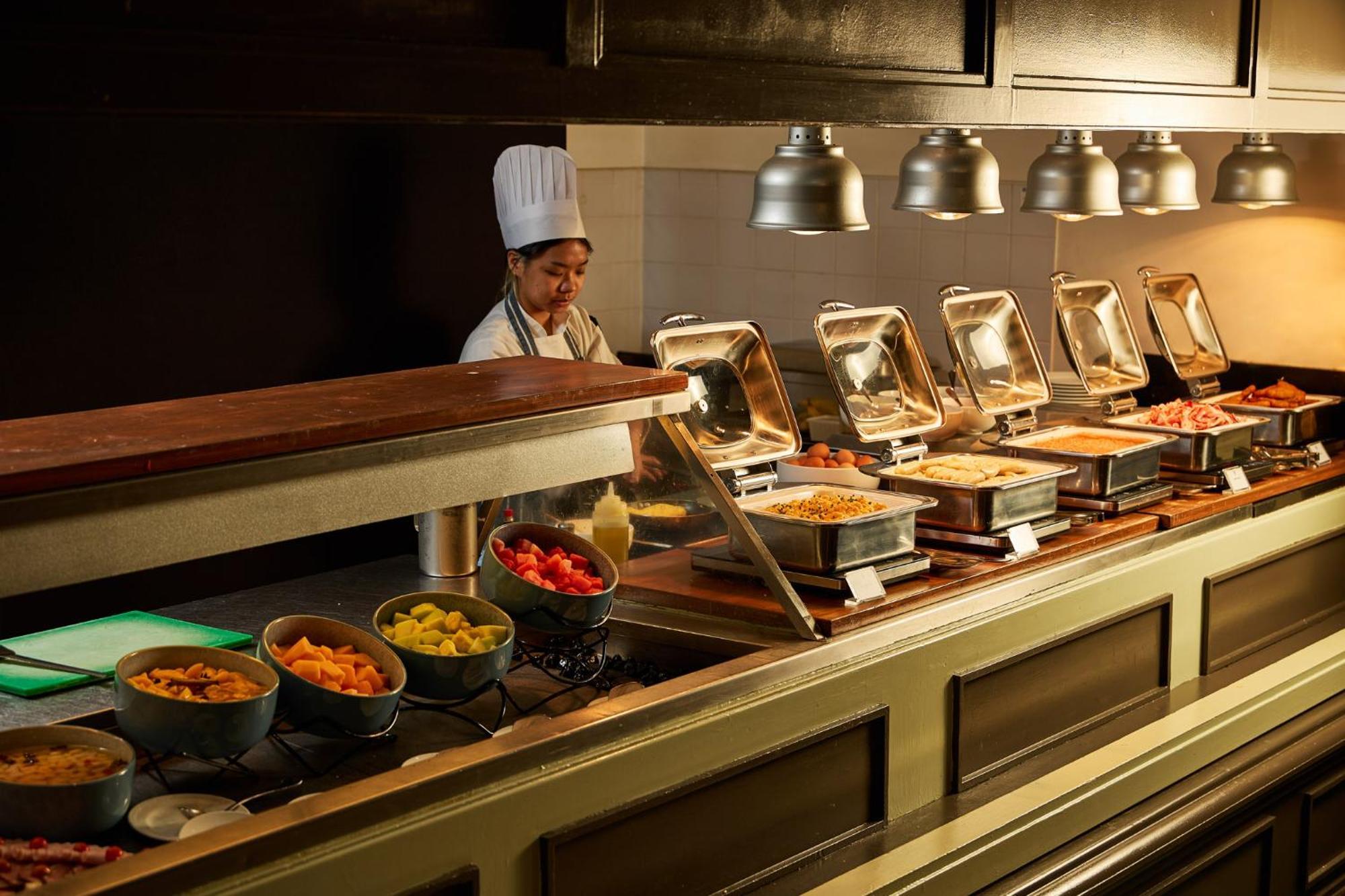 Stamford Plaza Melbourne Hotel Exterior foto The photo shows a buffet setup in a dining area. There is a chef in a white uniform and hat, standing behind a counter filled with various food options. The buffet features several metal serving trays containing different dishes, with warming lights 