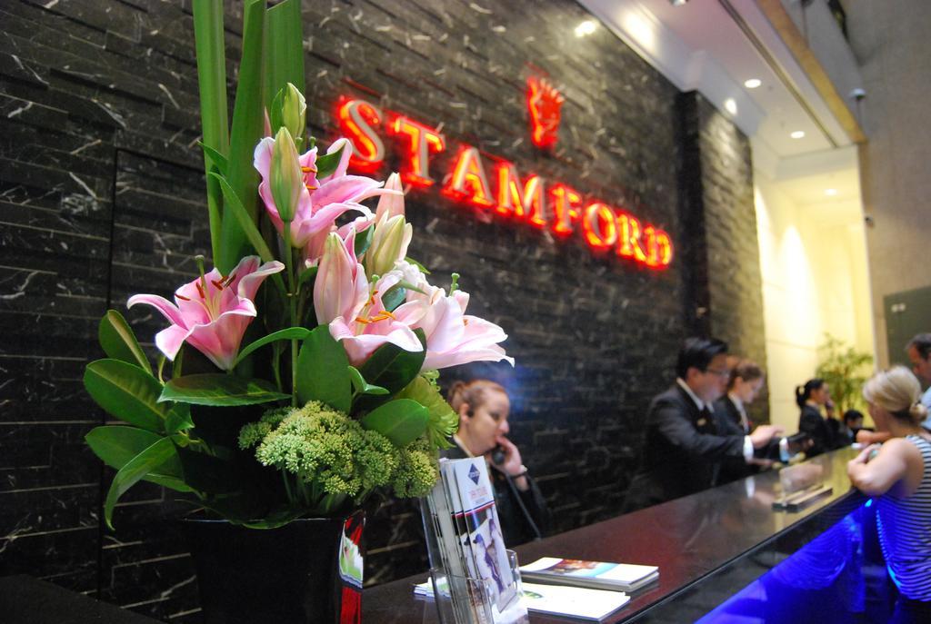 Stamford Plaza Melbourne Hotel Exterior foto The photo shows a hotel reception area with a prominent sign that reads "STAMFORD" in bright red letters. In the foreground, there is a decorative arrangement of flowers, primarily featuring pink lilies, along with greenery. The reception counter is 